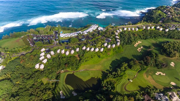 Vista aérea de un resort costero con múltiples alojamientos tipo bungalow, un campo de golf y una gran masa de agua.
