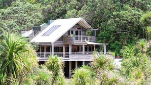 A two-story house with a balcony, surrounded by lush greenery and trees.