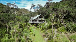 A two-story house with a balcony, surrounded by lush greenery and a clear sky.