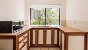 Cozinha com armários de madeira, micro-ondas embutido e janela com vista para o verde.