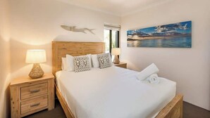 Quarto com cama, duas mesas de cabeceira, ventilador de teto, janela e um quadro na parede.
