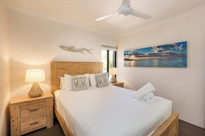 A bedroom with a bed, two bedside tables, a ceiling fan, a window, and a painting on the wall.