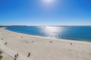 A beach with a clear sky, calm sea, and a few people walking.