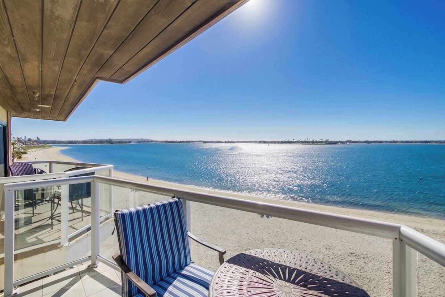 A balcony with a view of the sea, a chair, and a table.