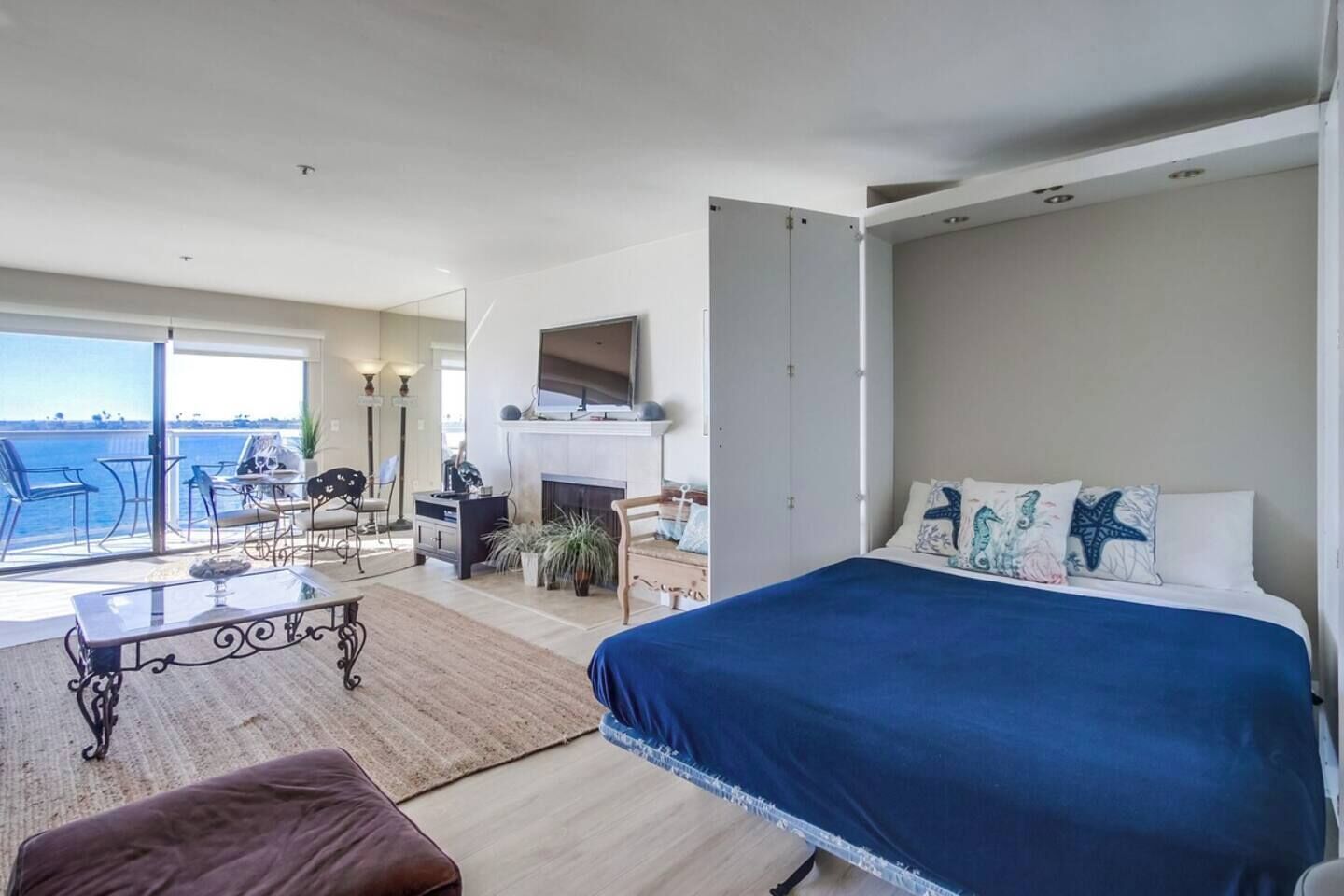 A bedroom with a bed, a desk, a chair, and a view of the sea.