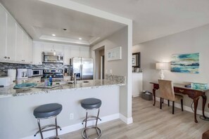A modern kitchen with stainless steel appliances, a marble countertop, and bar stools.