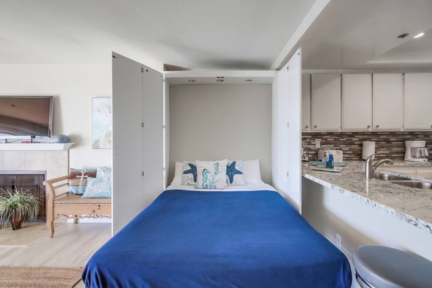 Quarto moderno com cama, TV, lareira e vista para a cozinha.