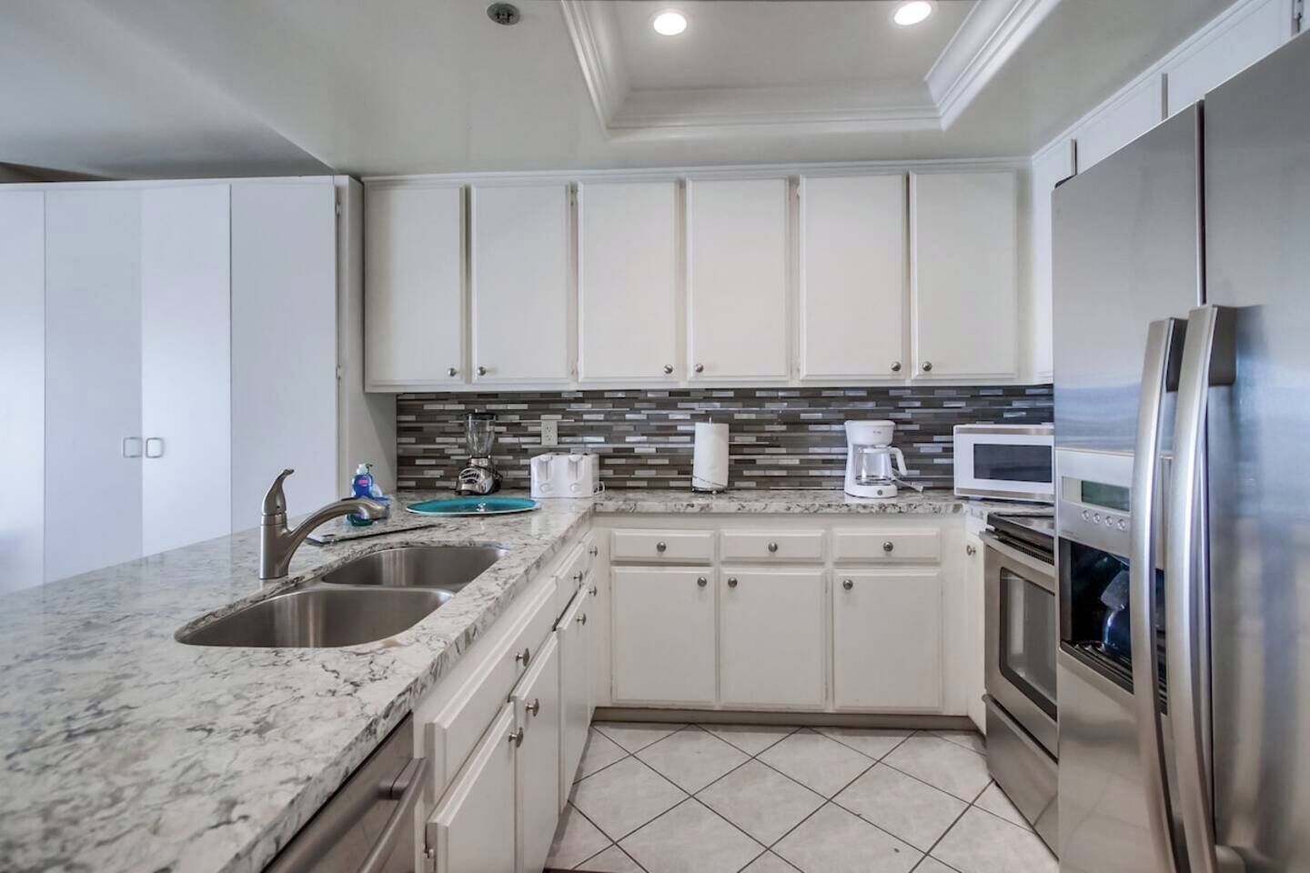 A modern kitchen with white cabinets, a granite countertop, stainless steel appliances, and a tiled backsplash.