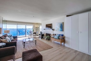 A spacious living room with a large window overlooking a body of water, a fireplace, and a seating area with a view.
