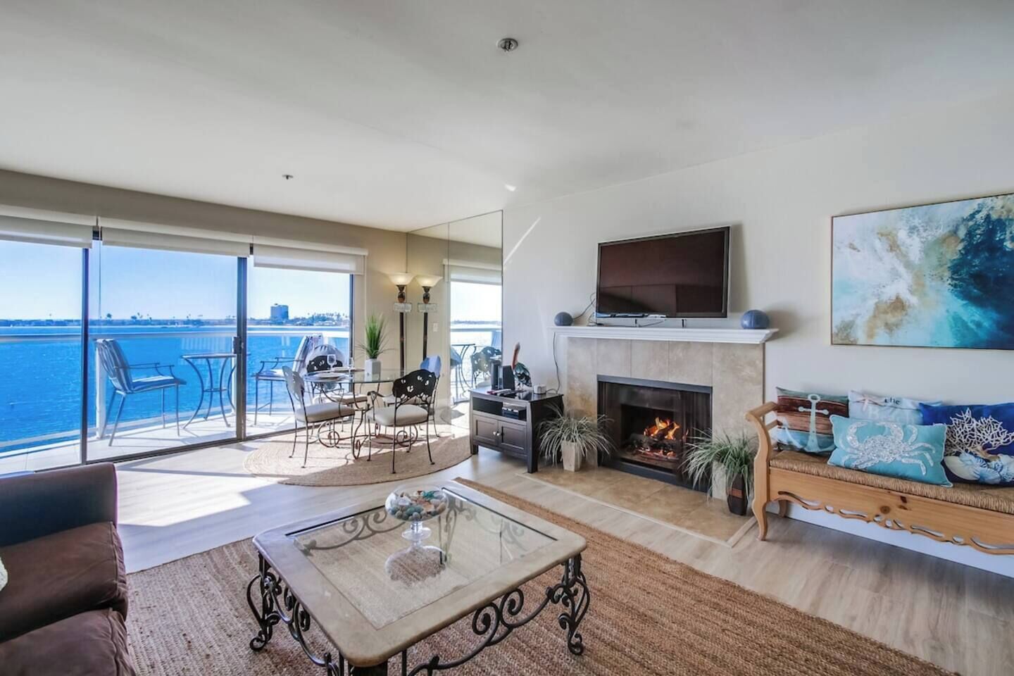 A spacious living room with a fireplace, a television, and a balcony with a view of the water.