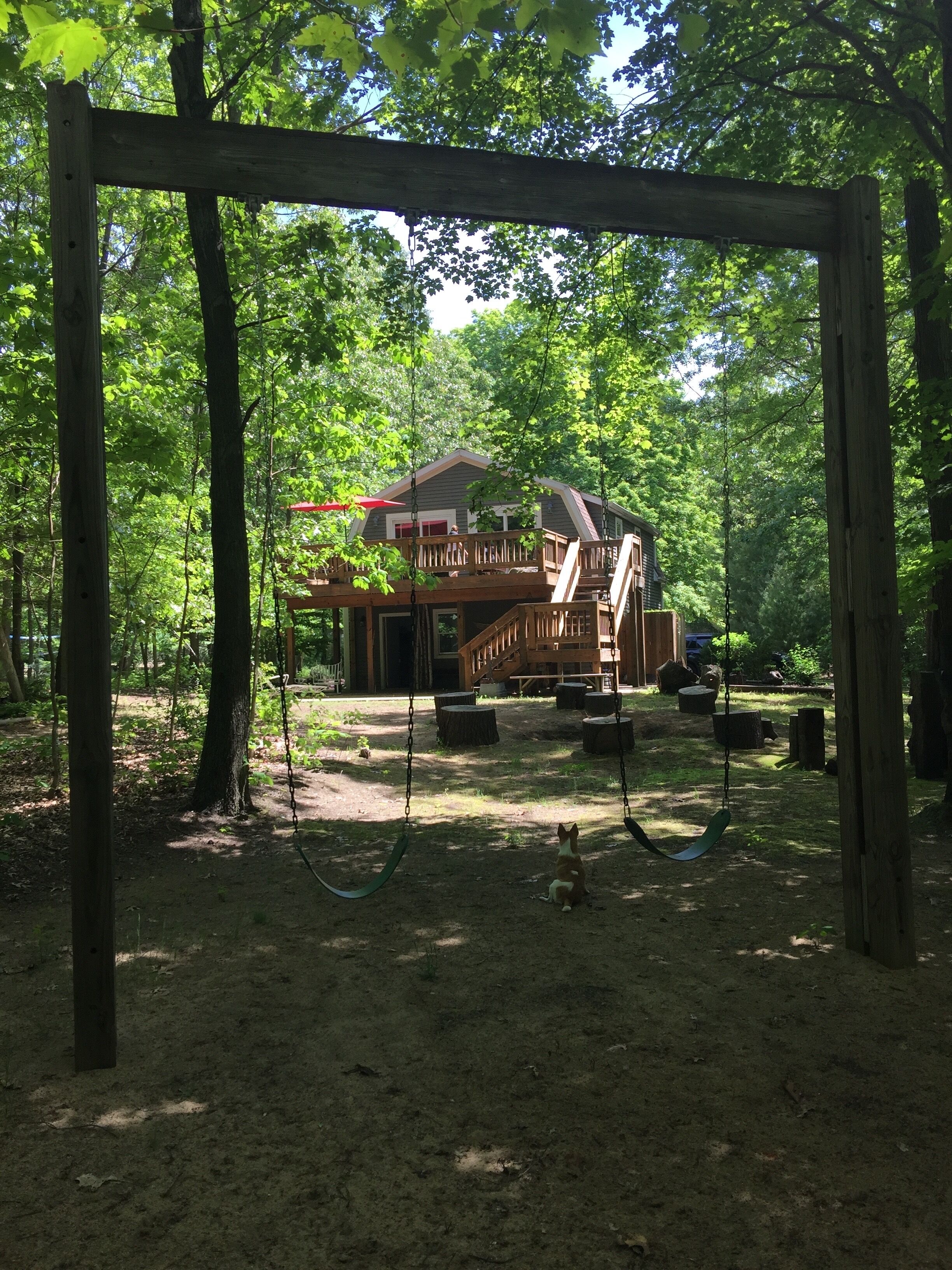 A wooden swing set in a wooded area with a house in the background.