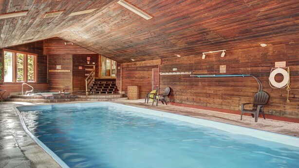 Een binnenzwembad met houten wanden en plafond, een jacuzzi en een trap naar een hoger gelegen niveau.