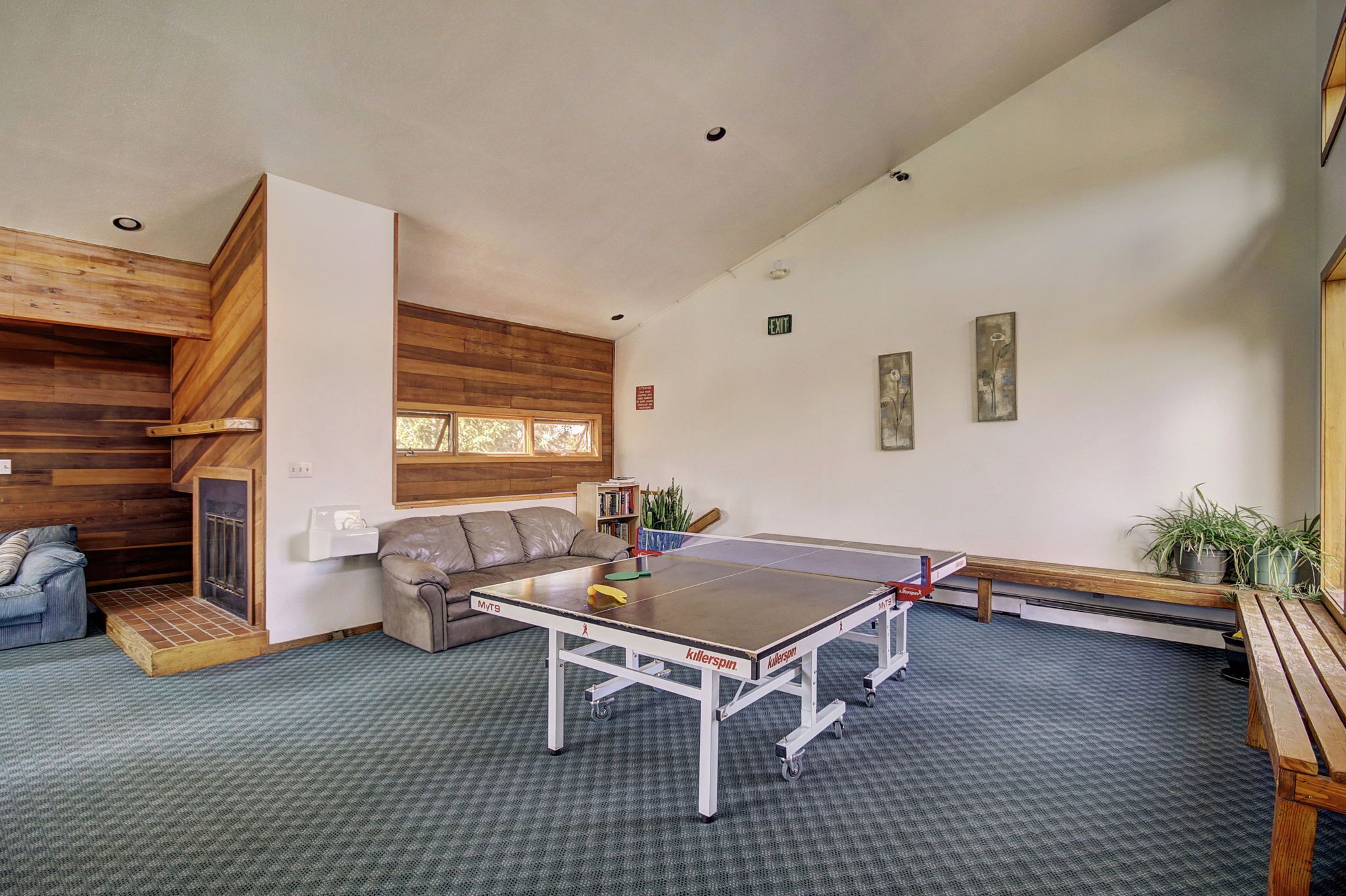 A ping pong table in a room with a wooden ceiling, a sofa, and a bookshelf.
