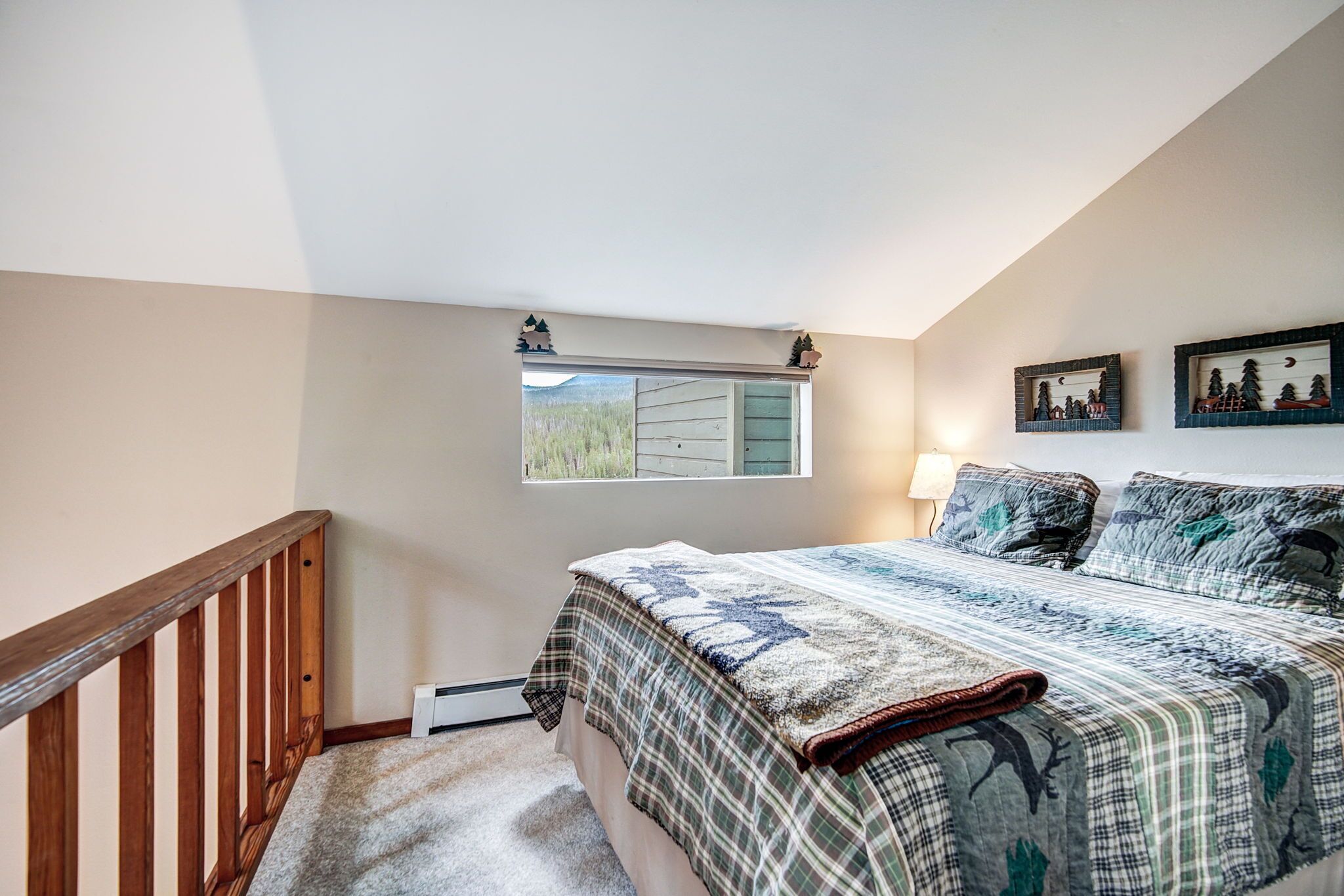 Een slaapkamer met een groot bed, een raam met uitzicht op de omgeving, een houten trap en een wandlamp.