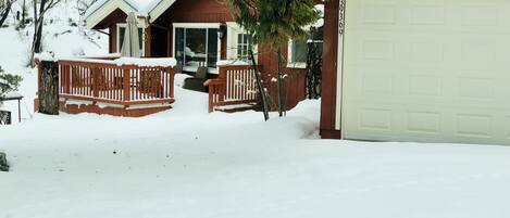 Una propiedad residencial con una terraza cubierta de nieve, un garaje y una casa de fachada marrón.