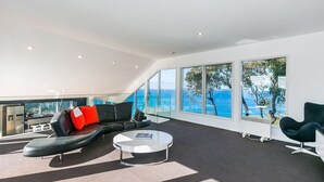Un salon moderne avec un canapé en cuir noir, une table basse blanche et une vue sur la mer grâce à de grandes fenêtres.