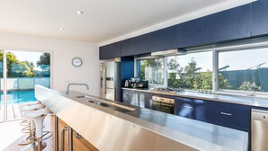 Une cuisine moderne dotée d’appareils électroménagers en acier inoxydable, d’une grande fenêtre et d’un coin bar aménagé près de la piscine.