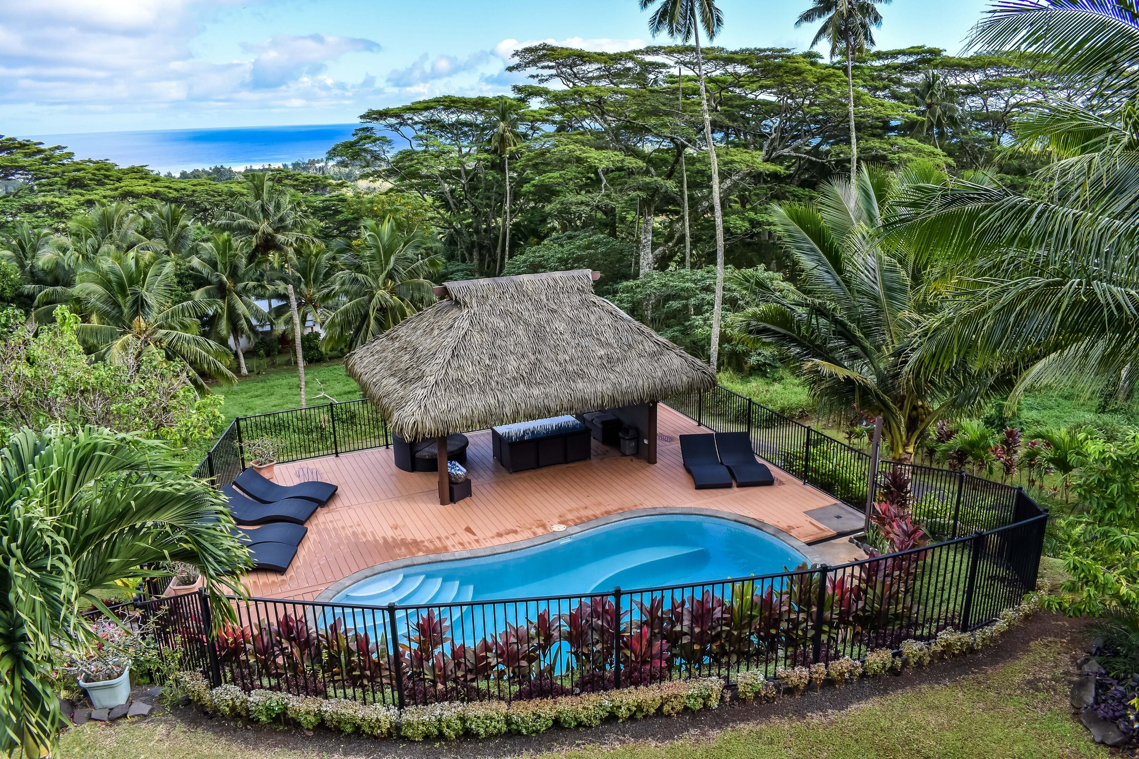 A pool area with a thatched-roof structure, lounge chairs, and a view of the ocean.