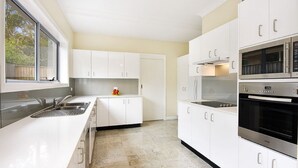 A modern kitchen with white cabinets, stainless steel appliances, and a large window providing natural light.