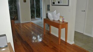A hallway with wooden flooring, a wooden table with a white object on it, and a door with a small window.