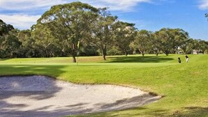 A golf course with a sand bunker, trees, and a clear sky.