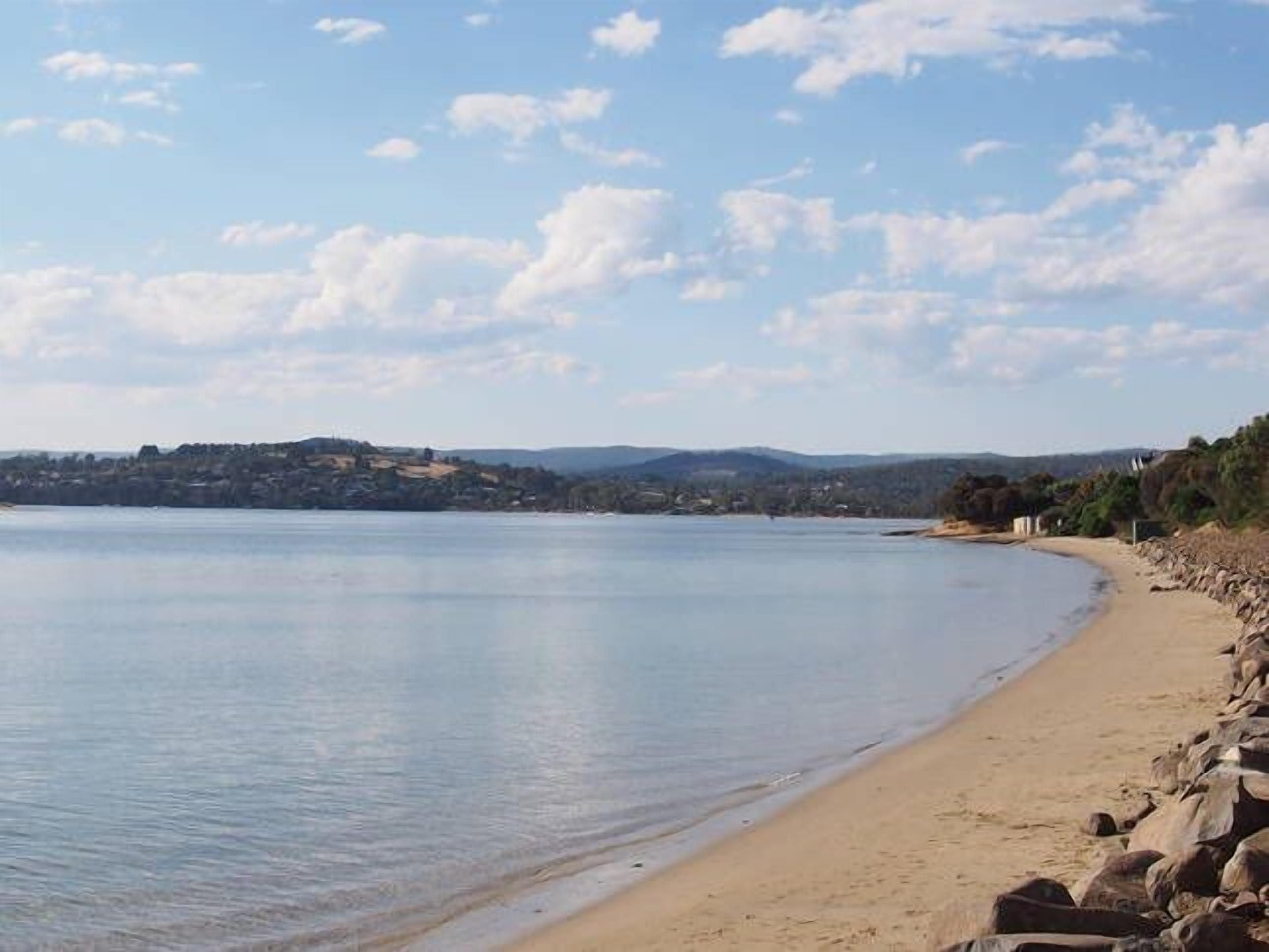 Une plage bordée d’une côte rocheuse, d’où l’on peut admirer des collines lointaines.