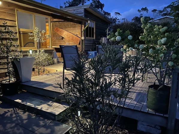 A wooden cabin with a patio area featuring a chair, potted plants, and a small table.