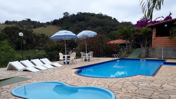 A swimming pool with lounge chairs and umbrellas, surrounded by stone tiles and greenery. - Chacara Dois Lagos!   Come and admire nature in this place!   (ITU)