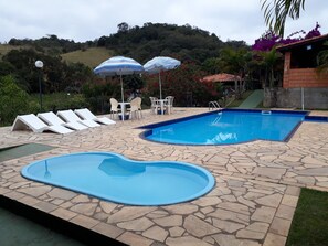 A swimming pool with lounge chairs and umbrellas, surrounded by stone tiles and greenery. - Chacara Dois Lagos!   Come and admire nature in this place!   (ITU)