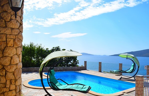 A swimming pool with two lounge chairs, one with a canopy, and a stone wall. - Seaside Villa, surrounded by pine forest with 34 m2 large heated swimming-pool. (Marina)