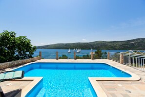 A swimming pool with a view of the sea and boats, surrounded by a stone wall and a metal railing. - Seaside Villa, surrounded by pine forest with 34 m2 large heated swimming-pool. (Marina)