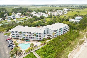 A multi-story hotel with a swimming pool, surrounded by lush greenery and a beach.