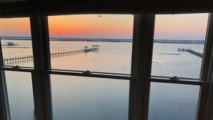 Vista a través de una ventana que muestra un cuerpo de agua tranquilo, un muelle de madera y una costa distante.