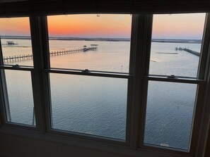 A view through a window with a view of a calm body of water, a wooden pier, and a distant shoreline.