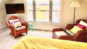 Un dormitorio con un amplio ventanal, muebles de mimbre, una cama y un televisor.
