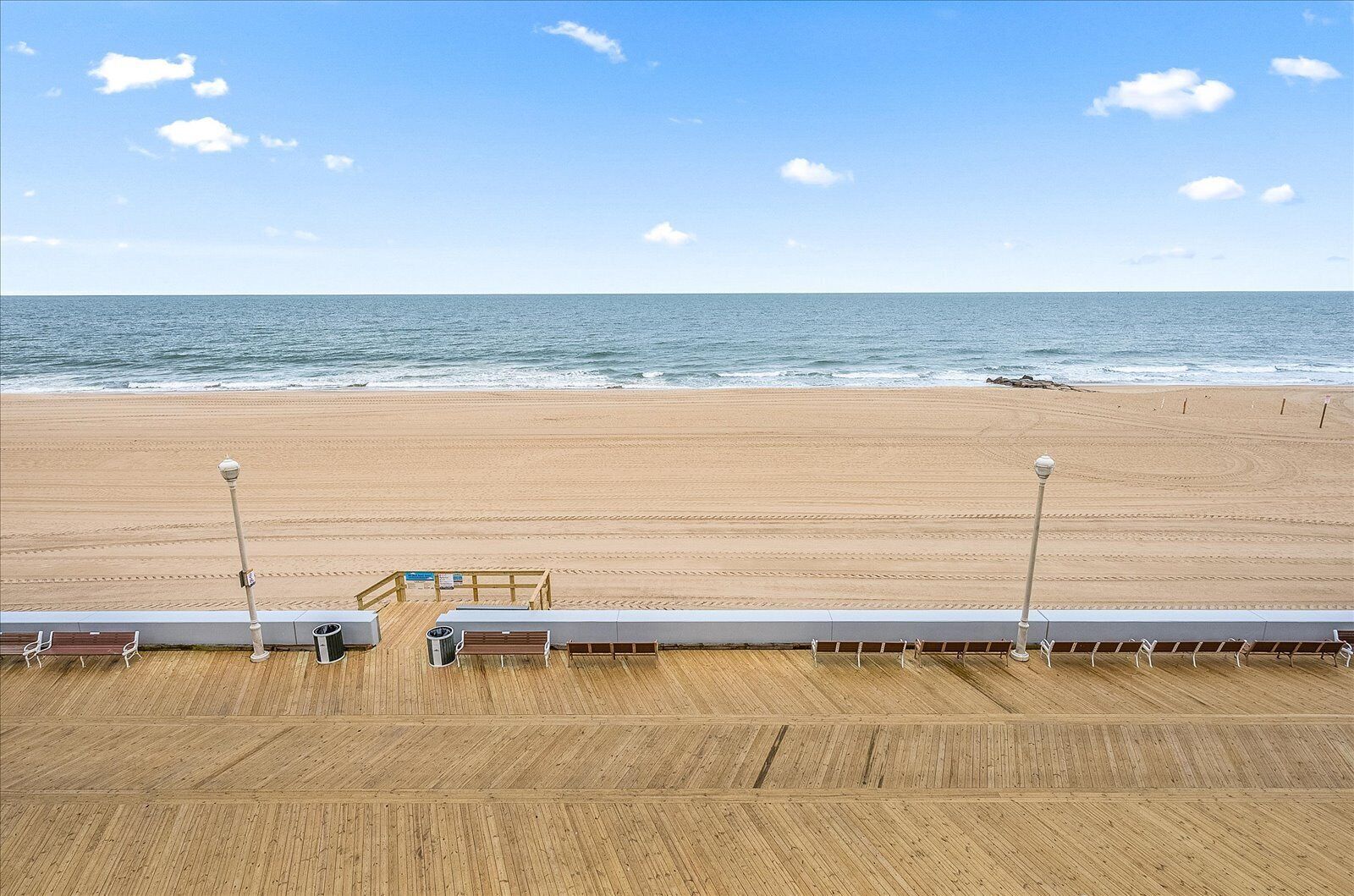 Une vue sur la plage depuis une terrasse en bois dotée d’une rambarde, d’une poubelle et de bancs.