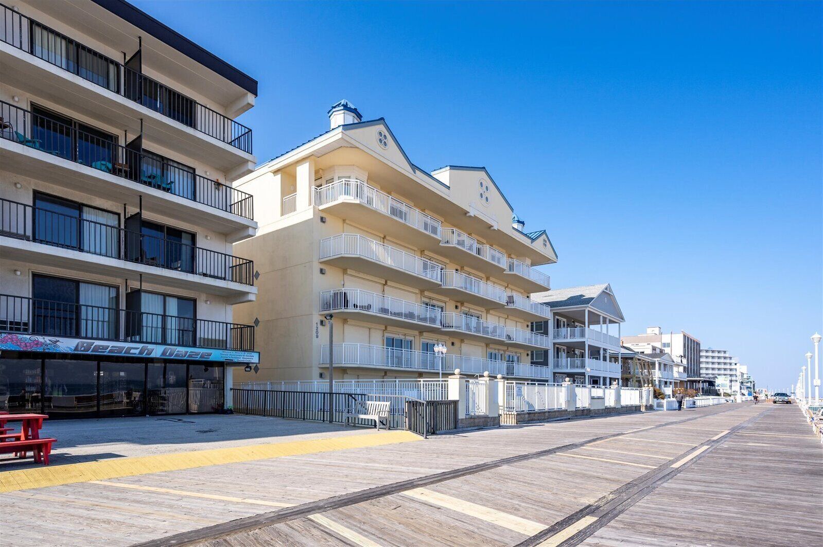 Um hotel à beira-mar com várias varandas, um calçadão e um restaurante na praia.