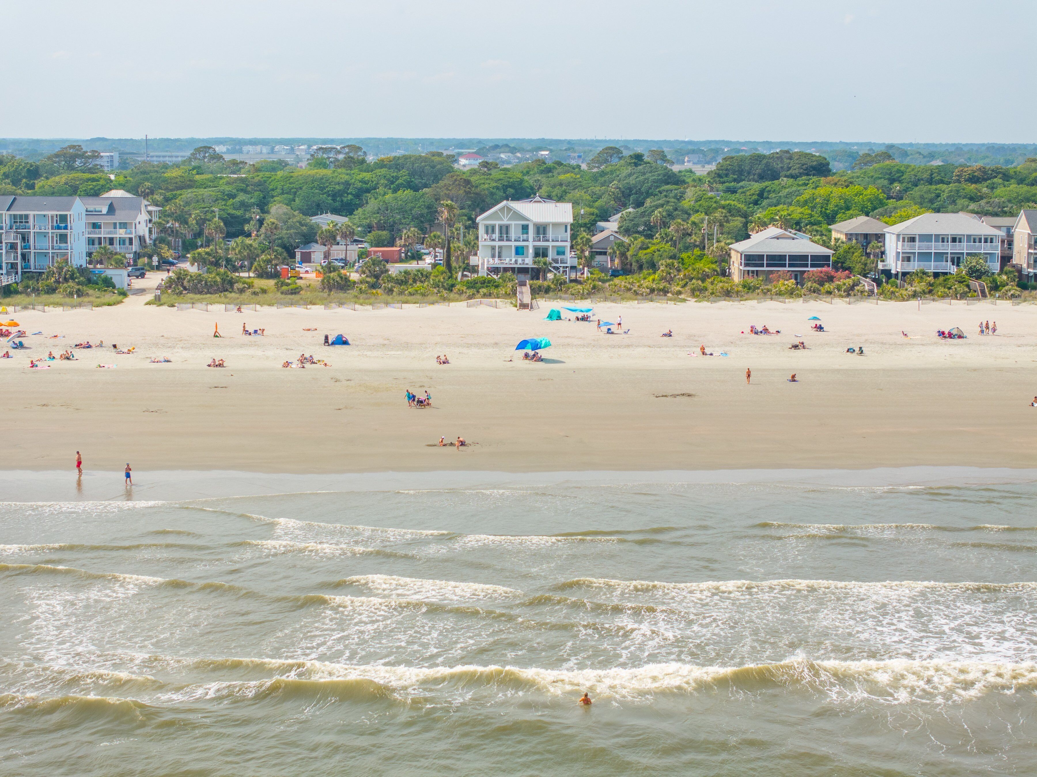 A beach with houses in the background and waves in the foreground.