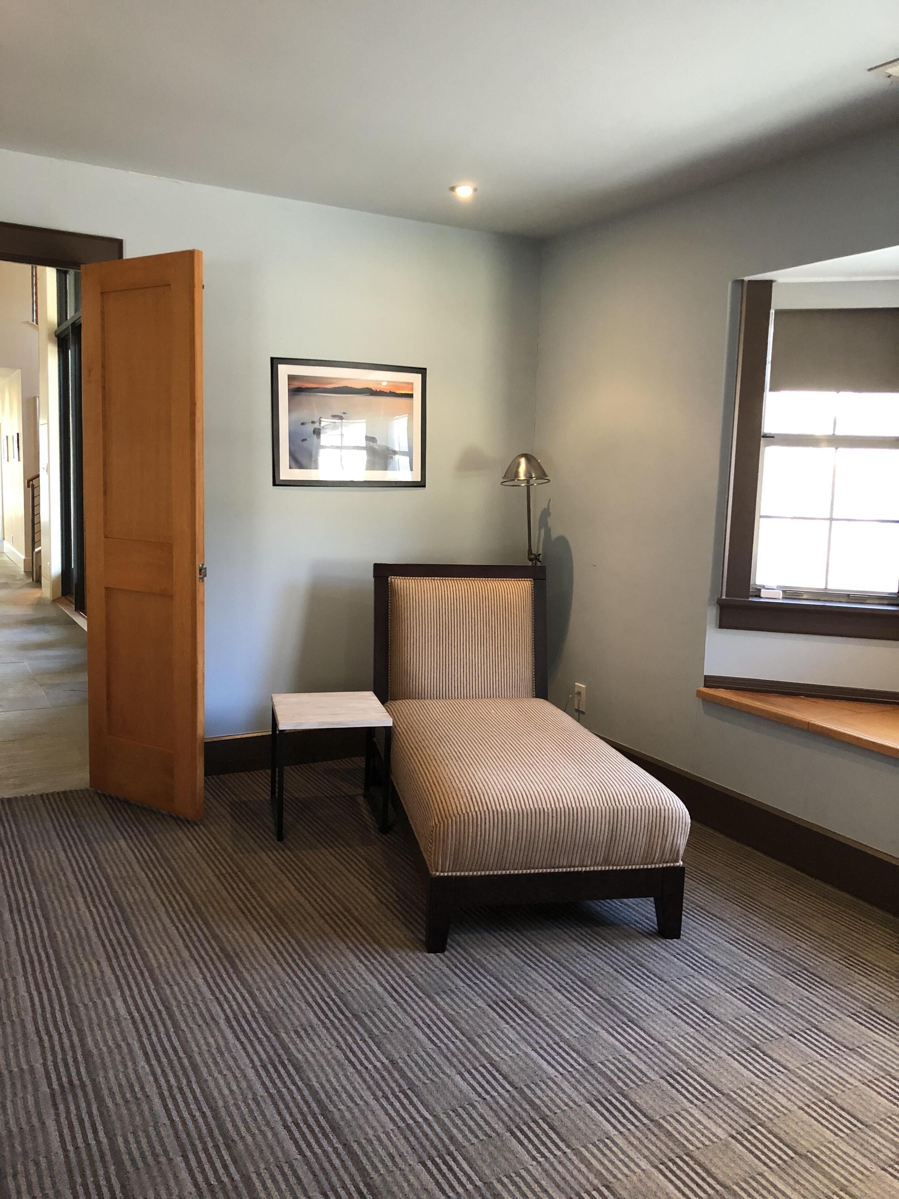 A small, neatly arranged room with a bed, a chair, a table, and a picture on the wall.