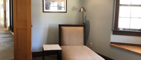 A small, neatly arranged room with a bed, a chair, a table, and a picture on the wall.