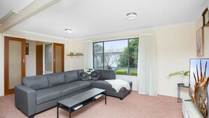 A modern living room with a grey sectional sofa, a coffee table, and a large window with curtains. - Great Location Stay and Relax (Victor Harbor)