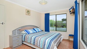 A bedroom with a bed, a bedside table, a small chair, a window with curtains, and a picture on the wall. - Great Location Stay and Relax (Victor Harbor)