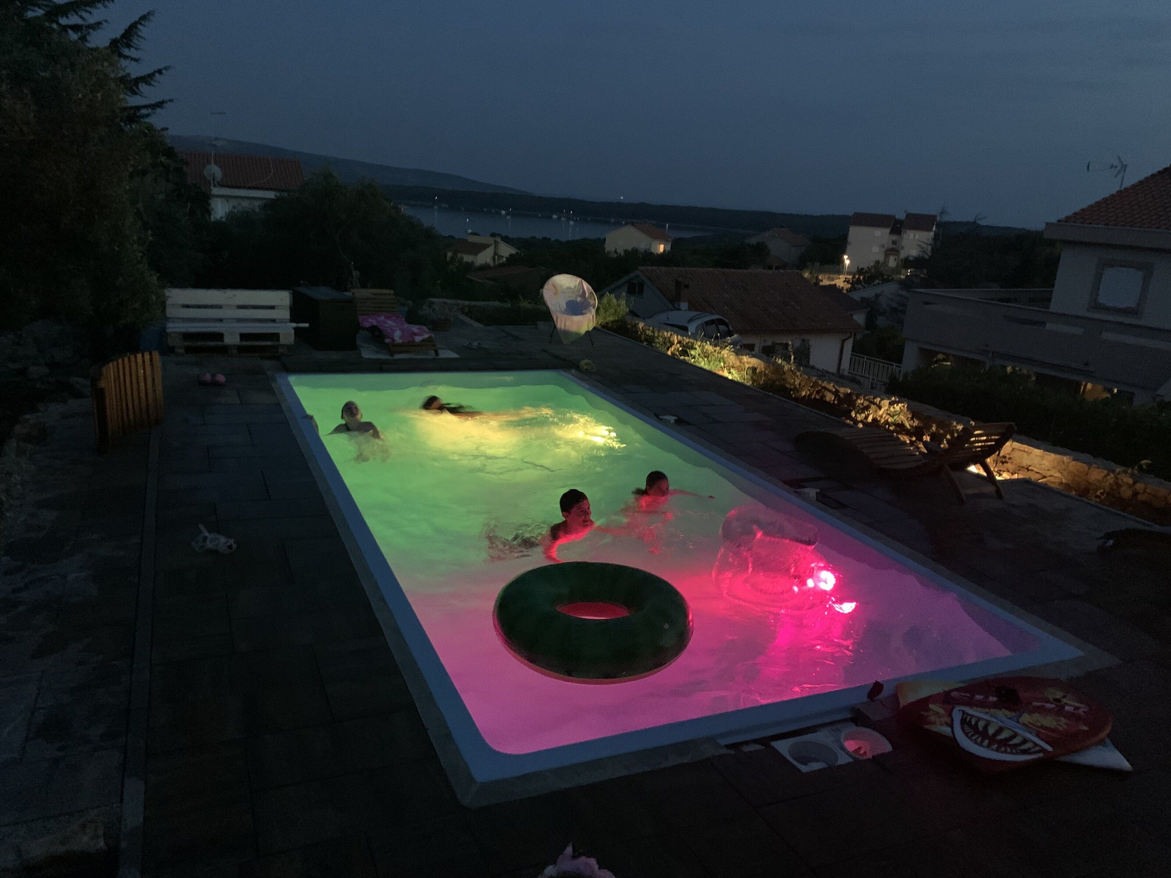 A rectangular swimming pool with a green inflatable ring in the center, surrounded by a stone deck.