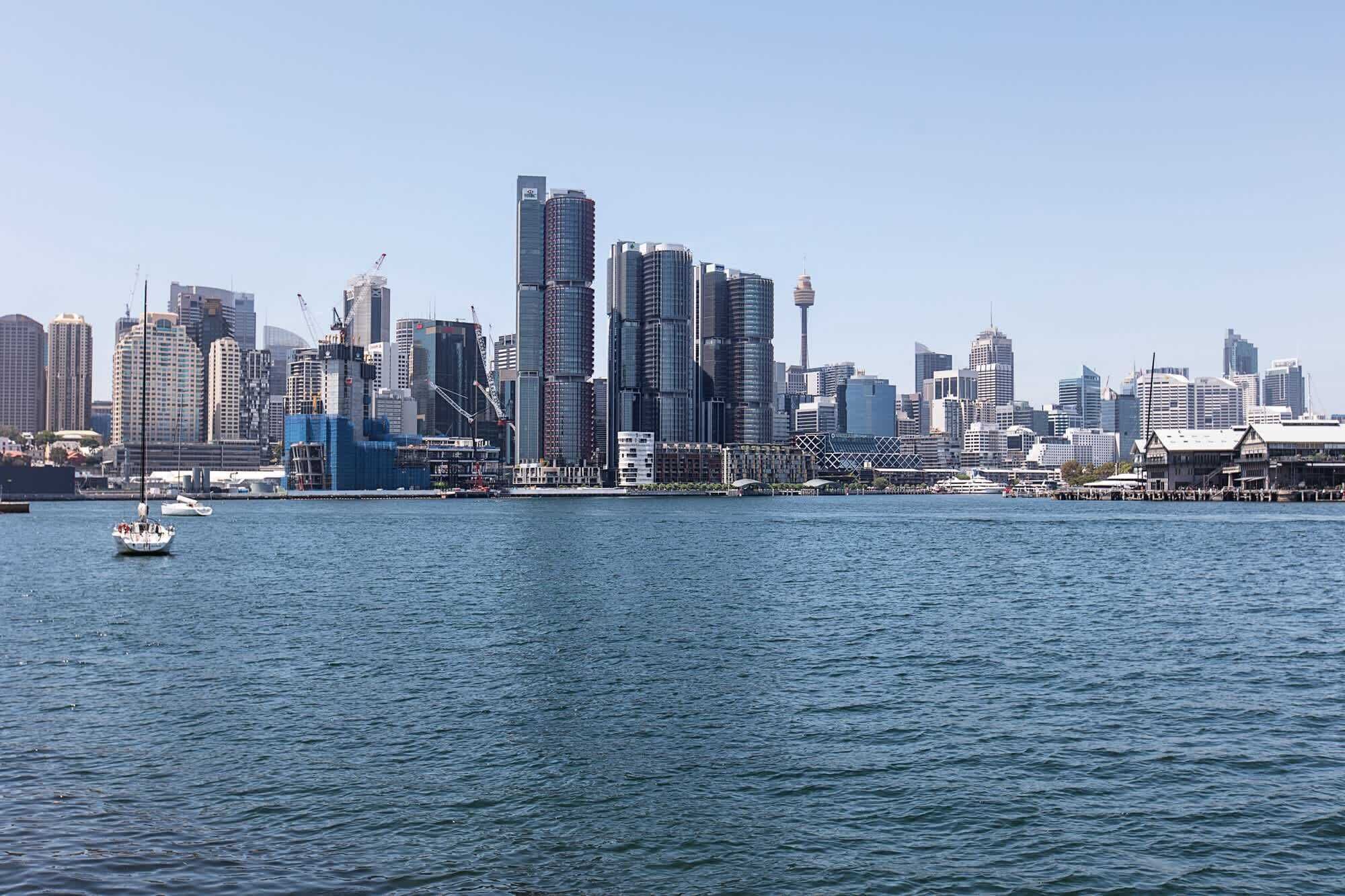 A city skyline with modern high-rise buildings, a waterfront, and a few boats on the water.