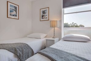 Habitación de hotel con dos camas individuales, una mesita de noche con lámpara y dos cuadros en la pared.