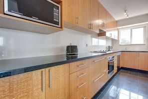 Una cocina moderna con armarios de madera, encimera negra, microondas, cafetera y lavavajillas.