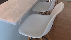 Una cocina con una encimera larga, sillas blancas y una zona de comedor con mesa y sillas.