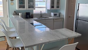 Una cocina con una isla central, taburetes de bar blancos, un refrigerador de acero inoxidable y una ventana con vistas.