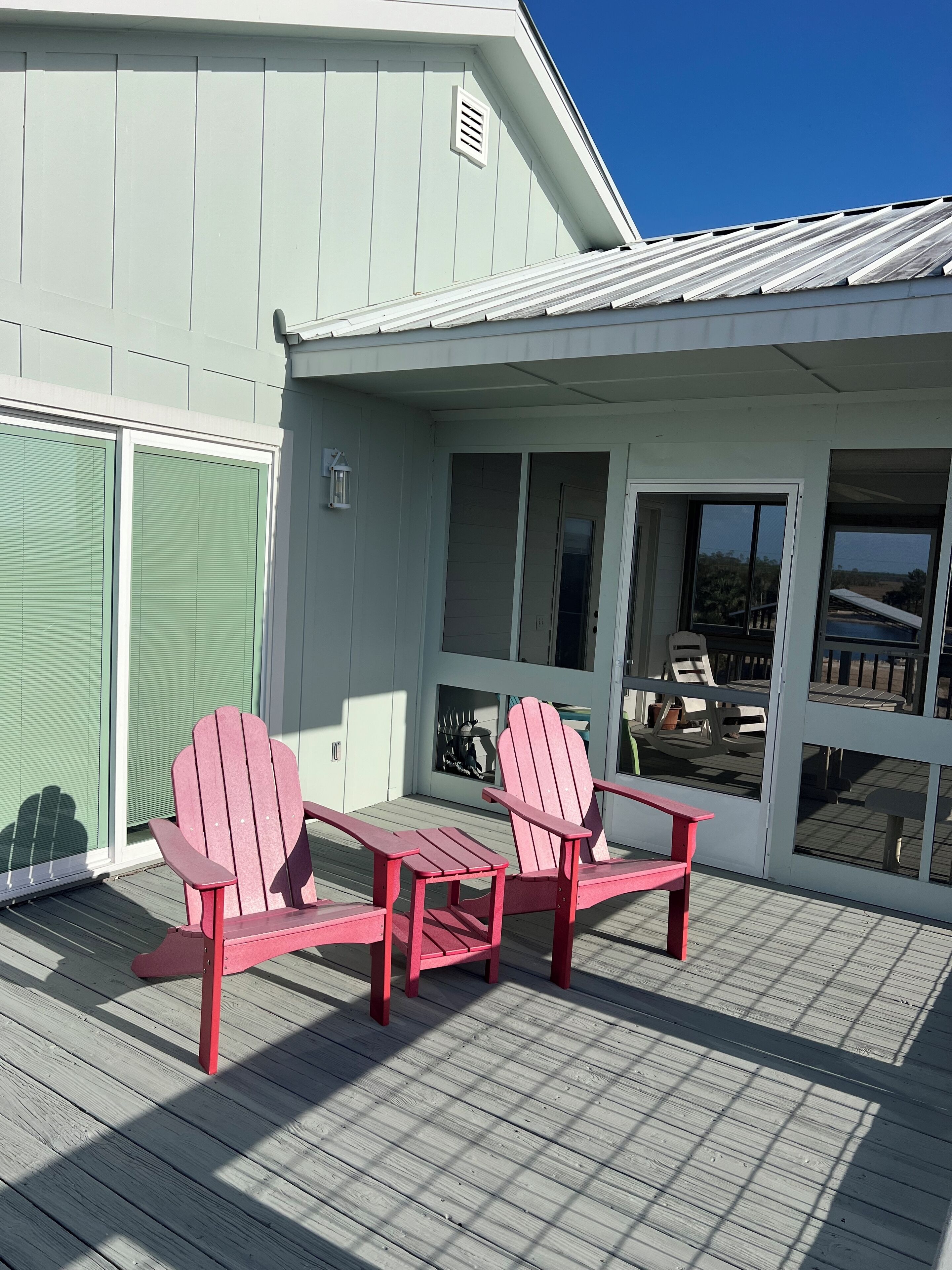 A covered deck with two red Adirondack chairs and a small table.