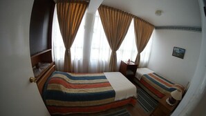 A room with two beds, a small table, and a chair. There is a window with curtains and a picture on the wall. - QUINTA VERGARA 5 PERSONAS  (Viña)